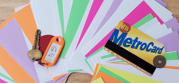 Colorful notecards fanned out on a table, accompanied by an old key on an orange keychain, a NYC MTA Metrocard, and an old NYC subway token